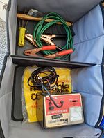 Wide view of the lot showing Morpower Deluxe battery charger and green jumper cables with copper clamps inside a soft container.