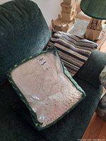 Green couch with packaged cream crocheted blanket and blue and white woven striped blanket on armrest.