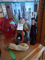 Collection of bottles and crystal decanter displayed on a wooden shelf, including red glass containers and some with wooden stands.