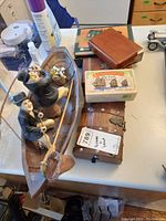 Image of wood boat with two Laurel and Hardy figurines fishing using rods, surrounded by wooden boxes and a mini soccer game box.