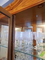 More than 10 crystal wine glasses with diamond cut pattern arranged on a shelf.