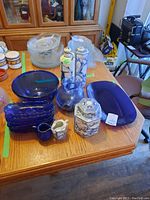 Overview of lot items on table including blue and white porcelain jars, blue glass vase, blue glass plates and bowl, creamers, large clear glass bowl, and dark blue glass dish.