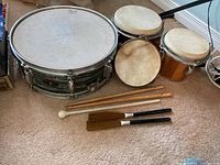 Overview photo showing snare drum, two bongos, tambourine, and drumsticks set out on carpet.