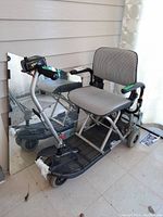 Full view of foldable electric mobility scooter showing the cushioned seat and armrests with black foot rest and metal frame.