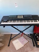 Full view of Yamaha PSR-330 keyboard on folding stand with manual on floor below. Shows keyboard keys, control panel, and general setup.
