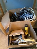 Two cardboard boxes containing electronic items including multiple cables, flashlights, and phones unearthed from boxes on the floor.