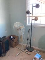 Photo showing Honeywell floor fan, black floor lamp, and black folding desk lamp bracket positioned near window