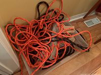 Coiled fire escape ladder with orange and black braided ropes and wooden rungs in a cardboard box.