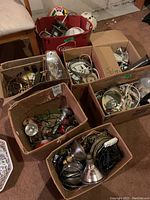 Boxes filled with assorted light fixtures, wiring, bulbs, and hardware on floor in basement setting