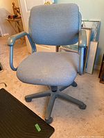 Front view of gray upholstered office chair with armrests and five caster wheels on carpeted floor.