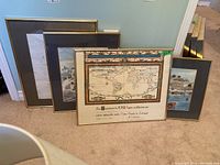 Four framed prints shown leaning against a wall, including a vintage world map and coastal scenes.