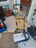 Front view of green Yardworks electric snow thrower with yellow extension cord wrapped around handle and owner's manual on top.