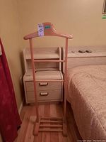Front view of wood valet stand positioned next to bed and nightstand.