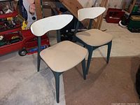 Two vintage wooden chairs with green legs, white curved wooden backs, and beige upholstered seats in basement setting
