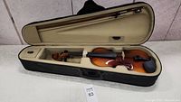 Child's violin laid inside zippered soft carrying case with bow secured above the instrument.