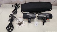 Two flash heads, two power cords, instruction manual and carrying case laid out