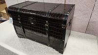 Front angle view of large dark brown vintage storage trunk with faux crocodile texture and brass rivets.