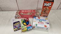 Lot overview showing five family games: Scrabble with damaged box, Jenga, Uno Flip, Charades for Kids, and Pie Face game