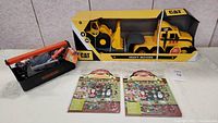 Full lot setup showing CAT construction truck in box, Black & Decker tool set in toolbox, and two Melissa & Doug puffy stickers sheets on a table.