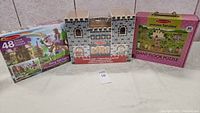 Wide photo of three items: Melissa & Doug Fold & Go Castle boxed in center, Fairy Tale Castle 48-piece puzzle on left, Princess Fairyland 60-piece puzzle on right.
