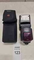 Sony HVL-F58AM flash and carrying case on table next to MaxSold lot tag