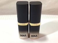 Two L'Oreal Colour Riche Gold Addiction lipsticks closed, showing the front with gold band and logo.