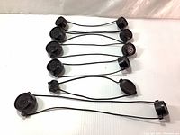 Photo showing seven pairs of black Bushnell scope lens caps connected by elastic cords arranged on white background.