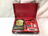 Open red detective briefcase displaying all included toy items: handbook, badge, magnifying glass, tweezers, stamps, evidence pot, chalk, and tape.
