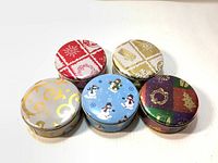 Front view of all five Christmas-themed round tin candy boxes showing different designs and colors.