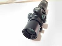 Close-up front view of the black matte Excalibur Tact Zone scope showing the large 32mm objective lens and light adjustment knob.