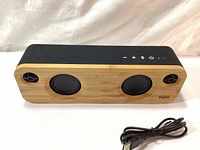 Front view of the speaker showing the bamboo wood panel with two main speaker drivers and two tweeters, along with control buttons on top.