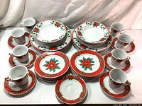 Full set displayed including plates, cups, and saucers with Christmas floral decoration and red borders