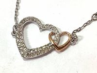 Close up of double heart pendant with crystals on silver-tone setting and attached smaller rose gold-tone heart.