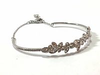 Front-angle view showing the curved rhodium-plated bangle with a floral pattern of clear Swarovski crystals and attached chain with lobster clasp.