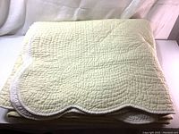 Folded quilt showing light lemon color and scalloped edges with white stitching