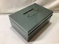 Closed view of vintage Oxford metal cash lock box with handle on top, muted green color, shows minor wear.