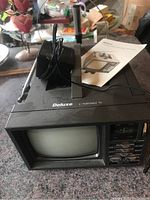 Front view of a Deluxe 8 inch portable analogue TV with power adapter and extendable antenna on top