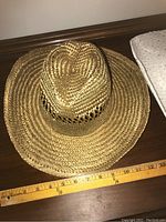 Natural woven straw sun hat with ventilation holes near crown and wide brim shown with ruler for size reference.