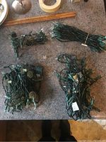 Four loose strands of Christmas lights showing green wiring and different bulb styles, some medium-size and some globe-shaped bulbs, coiled or bundled.