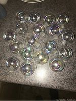 Eighteen clear glass round Christmas balls on a counter with iridescent shine.
