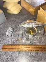 Clear crystal grand piano music box beside a ruler for size reference showing approximately 6 inches long. Small mechanical components visible inside.