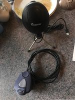 USB microphone on tripod and a small device with a cable (likely remote or receiver) shown on countertop.