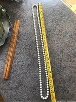 Photo of a pearl necklace next to a measuring tape and ruler on a flat surface showing necklace length and pearl details.