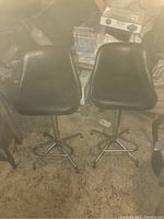 Pair of black swivel barstools with chrome bases seen from side angle in carpeted room
