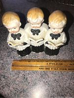 Front view of porcelain choir boys figurine, showing three boys holding songbooks and dressed in white robes with black bows.