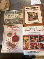 Four cookbooks lying flat, titles and covers visible, including farmhouse themed and modern cooking books.