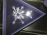 Close up of clear crystal snowflake ornament with star-shaped points inside blue triangular box, showing damage to the crystal points.