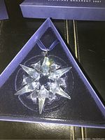 Clear Swarovski crystal Christmas ornament with pointed star-like design inside original blue triangular box