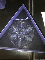 Top-down view of the crystal snowflake ornament in original triangular box with soft fabric lining.