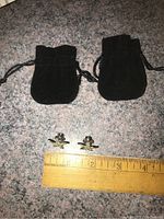 Photo showing the two starfish-shaped tac pins alongside black suede storage bags and a ruler for size reference.